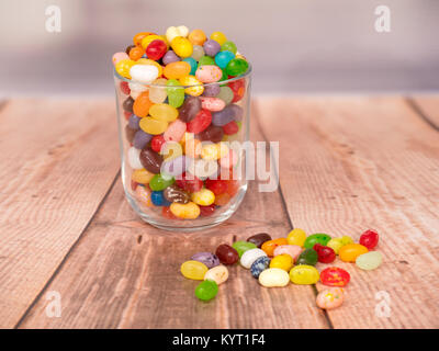 multicoloured jelly beans in a glass on a wooden background, with some spilled on the surface Stock Photo