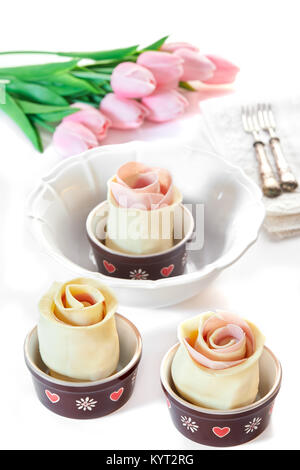 Puff pastry roses with ham and provola cheese in their casseroles, before being baked, on white table with pink tulips. Spring mood. Stock Photo