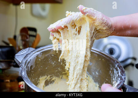 Cropped shot of hands knead dough on table, surrounded with much flour, bowls, eggs and milk. Professional chef works in bakery, preapares delicious H Stock Photo