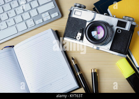 Open note pad, keyboard and vintage photo camera on a wooden desk. Mock-up. Stock Photo
