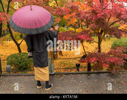 A man dressed in traditional Japanese clothes takes pictures of a woman at Kyoto's Eikando temple,  a popular destination as the autumn season. Stock Photo