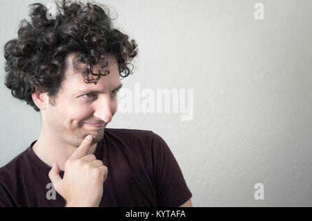 Portrait of a young, Caucasian, brunet, curly haired man with mocking expression on a white background. Stock Photo