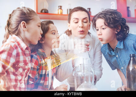 Work in team. Female chemistry teacher conducting a practical lesson with her pupils and involving them in the process of performing a chemical experi Stock Photo