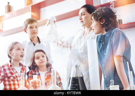 Can you see the reaction. Amazed up and coming chemists looking at a chemical reaction in a fuming filter flask held by a teacher of chemistry wearing Stock Photo
