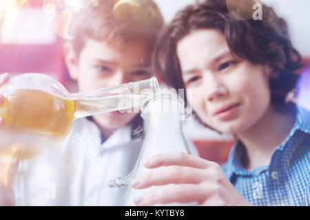 Add a little bit more. Two serious young chemist using different types of laboratory flasks while performing an experiment during a chemistry lesson a Stock Photo