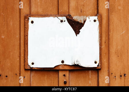 Empty rusty cracked and grungy white sign in rectangular shape weathered under the elements and fixed to an old red brown wooden wall with rusty nails Stock Photo