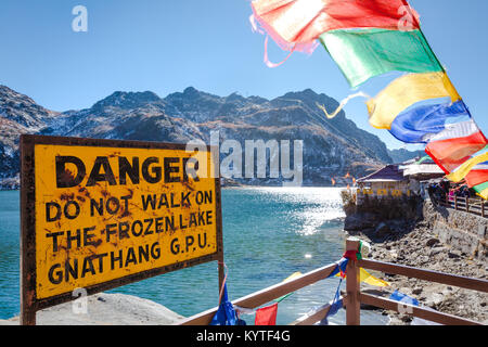 Tsomgo lake / Changu lake near Gangtok city in East Sikkim, North east India. Beautiful Buddhist prayer flags flutter and danger sign board in front Stock Photo