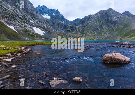 Friends fishing at Vishnusar lake on Kashmir great lakes trek in Sonamarg, India. Rocky terrain and  turquoise lake/tarn with snow mountains Stock Photo