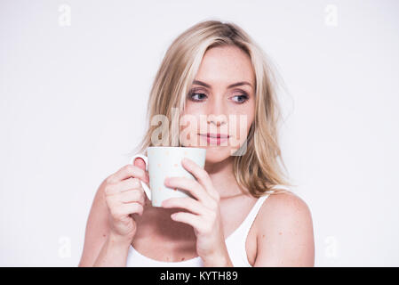 Beautiful young blonde woman drinking from a white mug Stock Photo