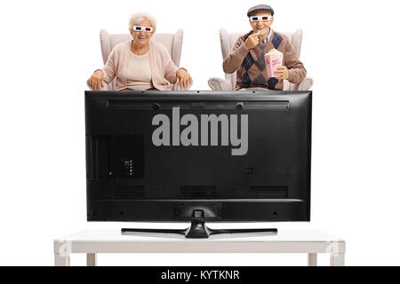 Seniors with 3D glasses and popcorn sitting in armchairs and watching television isolated on white background Stock Photo