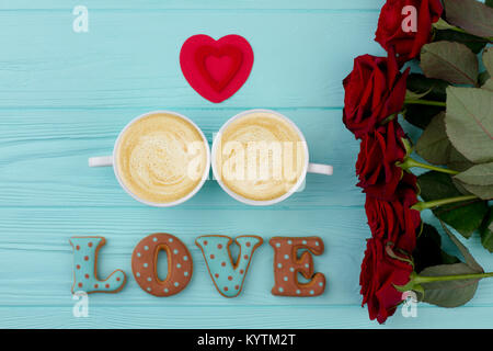 Coffee and roses, wooden background. Word love from baked cookies, two cups of coffee. Red heart and flowers. Celebration of Valentines Day. Stock Photo