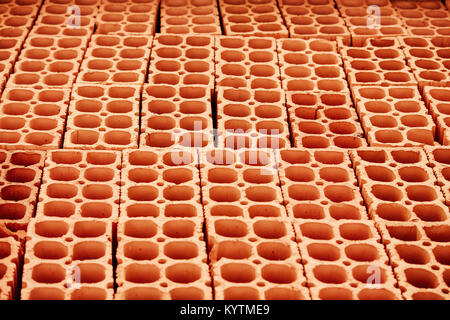 Pile of red hollow bricks with large holes forming lines in repeating geometric pattern similar to honeycomb background. Photo perspective from above.
