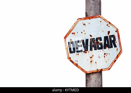 “Devagar” (in Portuguese, slow or slowly) written in a rusty and grungy white and red old weathered road traffic sign fixed to a concrete post and iso Stock Photo