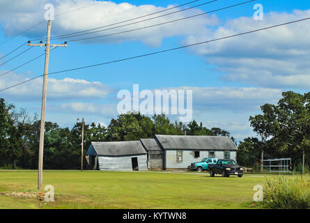 Abandoned derilict house with windows missing in rural America with two pickup trucks parked outside and a tree with a tire swing Stock Photo