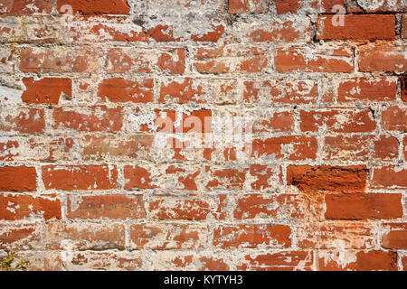 An old weathered, damaged, formerly painted, badly repaired red brick wall full frame background Stock Photo