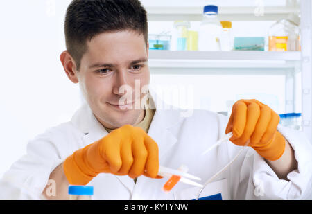 Young male scientist or tech in white coat and orange protective gloves works with liquid sample in cryovia in research laboratoryl. Stock Photo