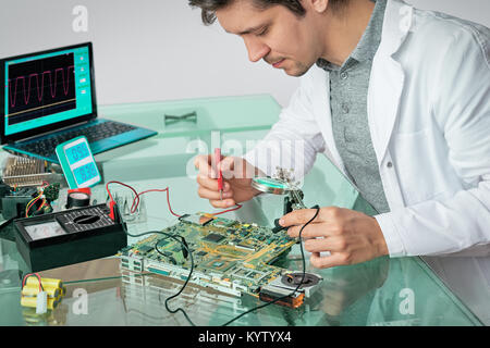 Young energetic male tech fixes laptop motherboard, shallow DOF, focus on the eyelashes Stock Photo