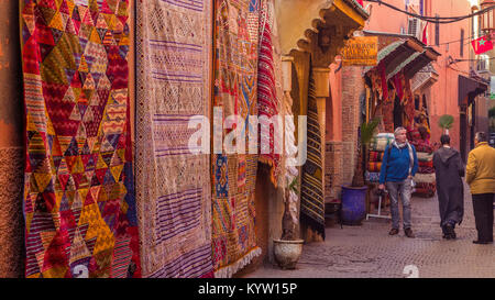 Male tourist walks through street with rugs and carpets on display in the shops in the souk in the ancient Medina of Marrakesh, Morocco Stock Photo