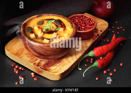 Spicy pumpkin soup in wooden bowl on dark background, served with pumpkin oil, pumpkin seeds, croutons and thyme leaves. This is German variation of p Stock Photo
