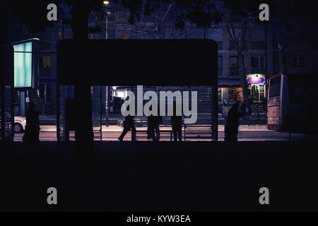 A night city scene, a bus stop with a couple of waiting passengers. The bus passed, winter on the street. Stock Photo