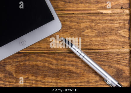 Digital tablet computer and ballpoint pen are placed on a wooden table background Stock Photo