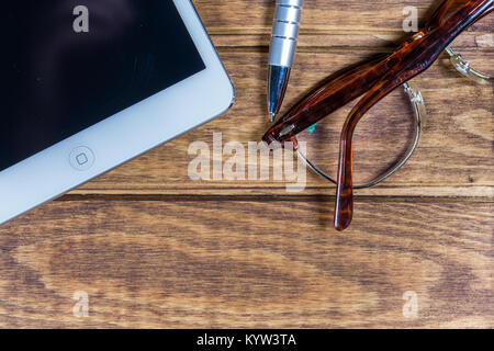 Digital tablet computer,Eyeglasses and ballpoint pen on Wood.Top View Stock Photo