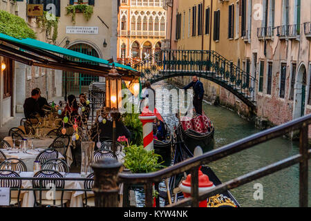 Man with a gondola passes an outdoor restaurant terrace by a canal in Venice, Italy. Stock Photo