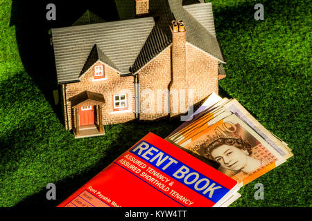 Model house, rent book (for assured shorthold tenancy, in England and Wales) and pounds sterling notes. General concept of renting / letting a home. Stock Photo