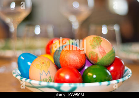 Easter eggs painted by children themselves in a fine Gmundner Keramik porcelain from Austria on a table set with wine glasses. Stock Photo