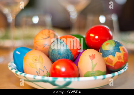 Easter eggs painted by children themselves in a fine Gmundner Keramik porcelain from Austria on a table set with wine glasses. Stock Photo