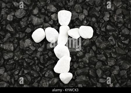 Cross of white pebbles against background of black grit Stock Photo