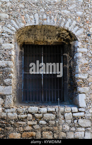 Arched window with bars set in deep rustic rock wall Stock Photo