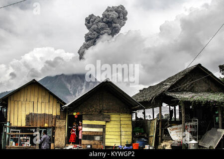 Karo, North Sumatra, Indonesia. 16th Jan, 2018. Young Indonesian girls play in front of their house as the Mount Sinabung volcano spreads volcanic ash to the sky, in Karo, North Sumatra. Mount Sinabung roared back to life in 2010 for the first time in 400 years, after another period of inactivity it erupted once more in 2013, and has remained highly active since. Credit: Ivan Damanik/ZUMA Wire/Alamy Live News Stock Photo