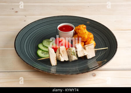 Pieces of chicken fillet on skewer with fried potato balls and vegetables Stock Photo