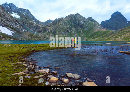 Friends fishing at Vishnusar lake on Kashmir great lakes trek in Sonamarg, India. Rocky terrain and  turquoise lake/tarn with snow mountains Stock Photo