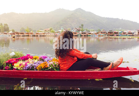 A Shikhara full of colorful flowers with a single travelling girl/woman. Backpacking girl on Dal lake, Srinagar, Kasmir, India. vibrant sunrise scene, Stock Photo