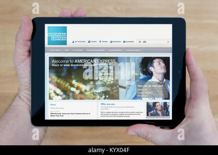 A man looks at the American Express website on his iPad tablet device, with a wooden table top background (Editorial use only) Stock Photo