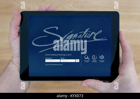 A man looks at the Signature Bank website on his iPad tablet device, with a wooden table top background (Editorial use only) Stock Photo