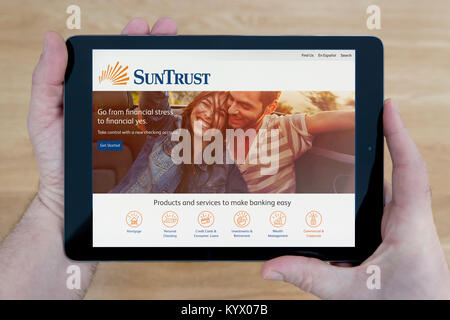 A man looks at the SunTrust Bank website on his iPad tablet device, with a wooden table top background (Editorial use only) Stock Photo