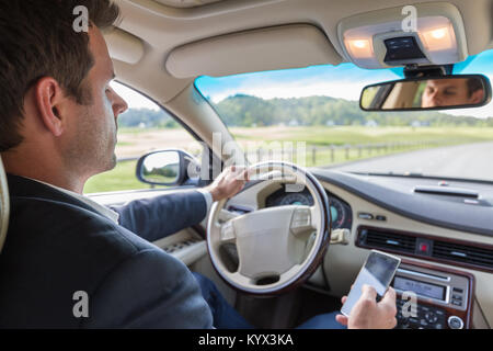 Businessman using cell phone and texting while driving not paying attention to the road. Stock Photo
