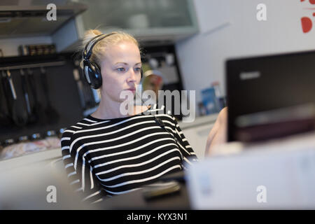 Adult woman in her casual home clothing working and studying remotely from her small flat late at night. Stock Photo