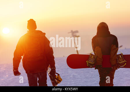 Two snowboarders walking against sunset sky Stock Photo