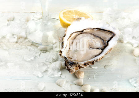 A closeup photo of a freshly opened oyster on ice, with a glass of wine, a slice of lemon, and a place for text. Selective focus Stock Photo