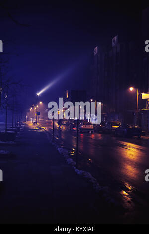 Small Balkan town in winter, at night, with fog and some passerby. Stock Photo