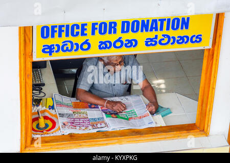 KANDY, SRI LANKA - FEBRUARY 8: Man sitting in the donation office and reading newspaper at the white Buddha temple waiting for people to make a donati Stock Photo