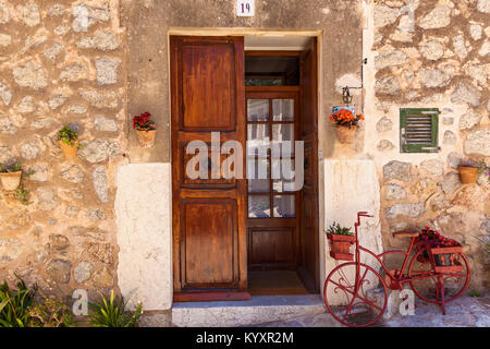 A red bicycle, loaded with flowers, stands in front of an old wooden door in the traditional Spanish medieval city center.Palma de Mallorca Stock Photo