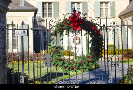 Christmas wreath on Gate framing matching door wreath in distance at upscale residence Stock Photo