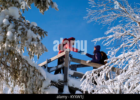 two people on an equipped trail in the winter mountains; the man holds out his hand to the woman, helping to climb up the slippery steps Stock Photo