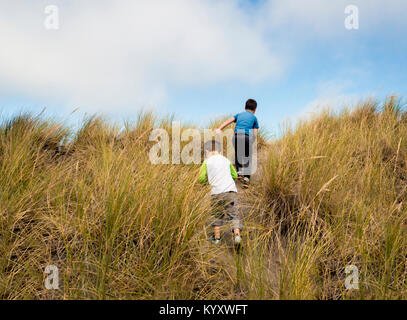 Rear view of siblings walking on trail amidst grass against sky Stock Photo