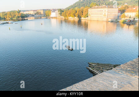 PRAGUE CZECH REPUBLIC - AUGUST 229,2017; Auntumn colors and buildings on side of Vltava River caught in sunrise while man fishes from boat fr Stock Photo